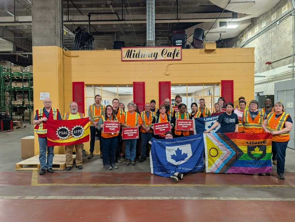 UNDE members in high-visibility vests holding "Support our bargaining team" signs, with UNDE and PSAC flags